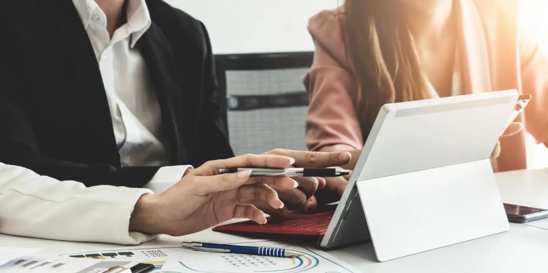 Business professionals collaborating over a tablet, discussing strategic growth solutions, with documents and pens on a table.