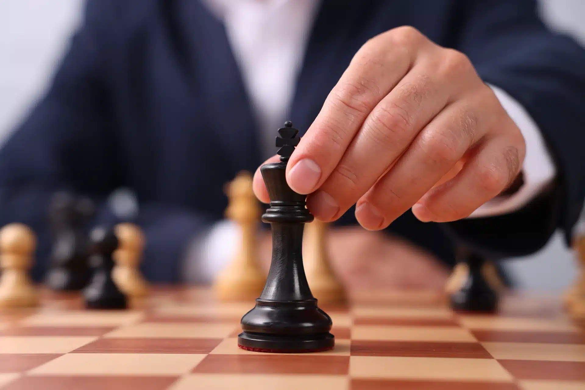 Business professional moving a black king chess piece on a chessboard, symbolizing strategic decision-making in political campaign consulting.