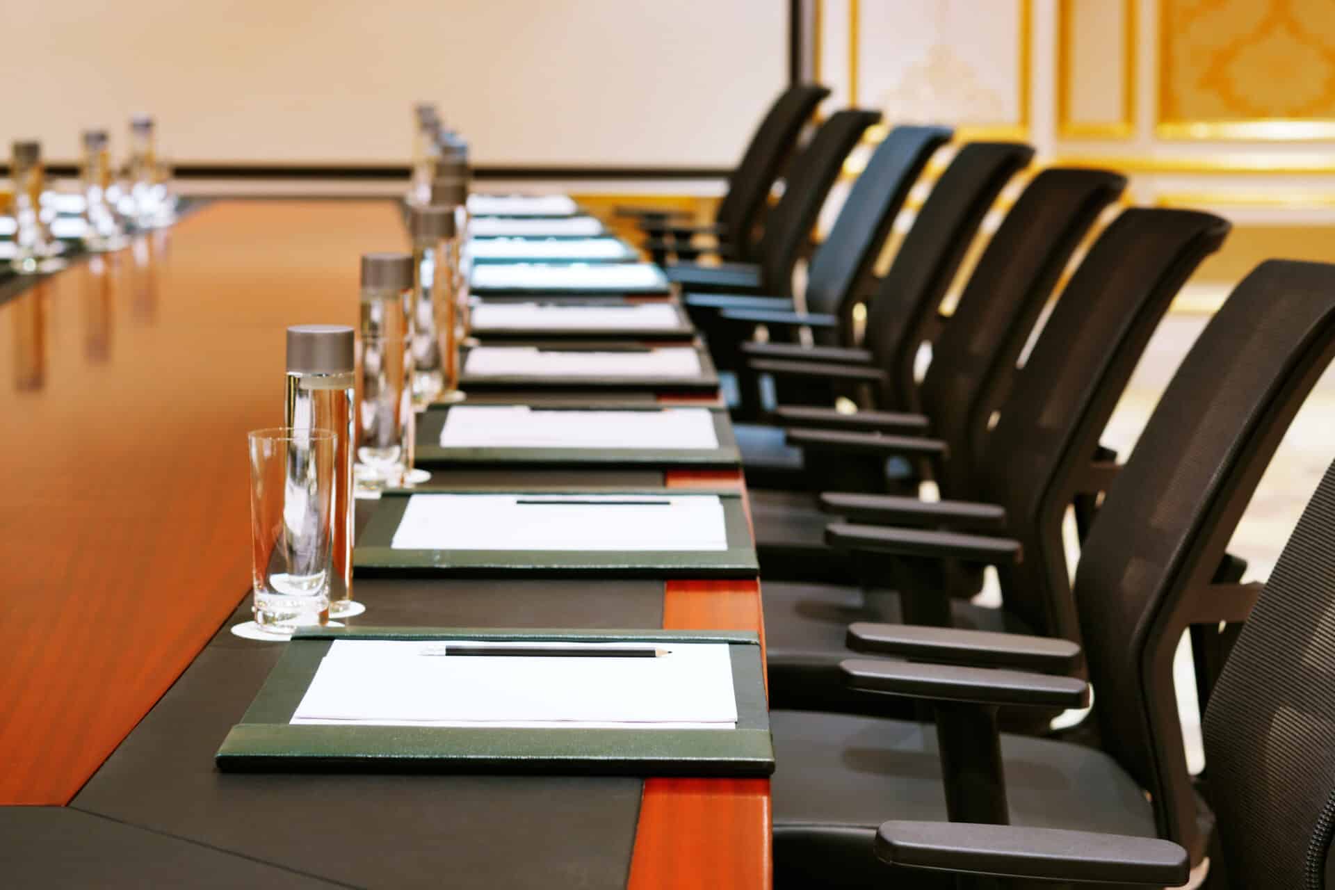 Conference room setup with a long wooden table, black ergonomic chairs, water bottles, and notepads, reflecting a professional environment for corporate meetings and marketing strategy discussions.