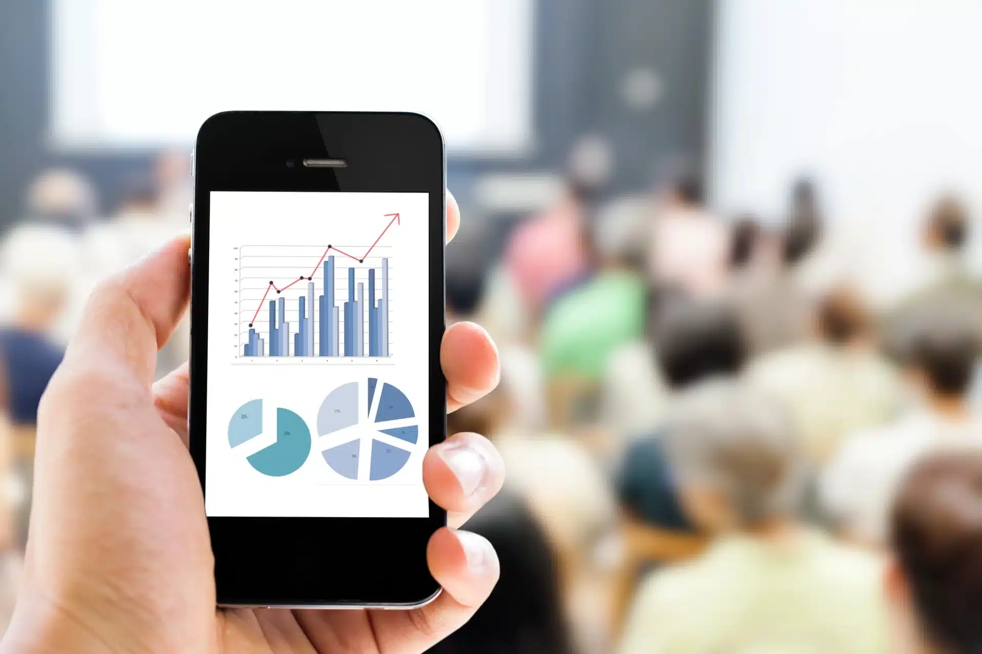 Hand holding smartphone displaying market research graphs and charts, symbolizing data-driven decision-making for small businesses.