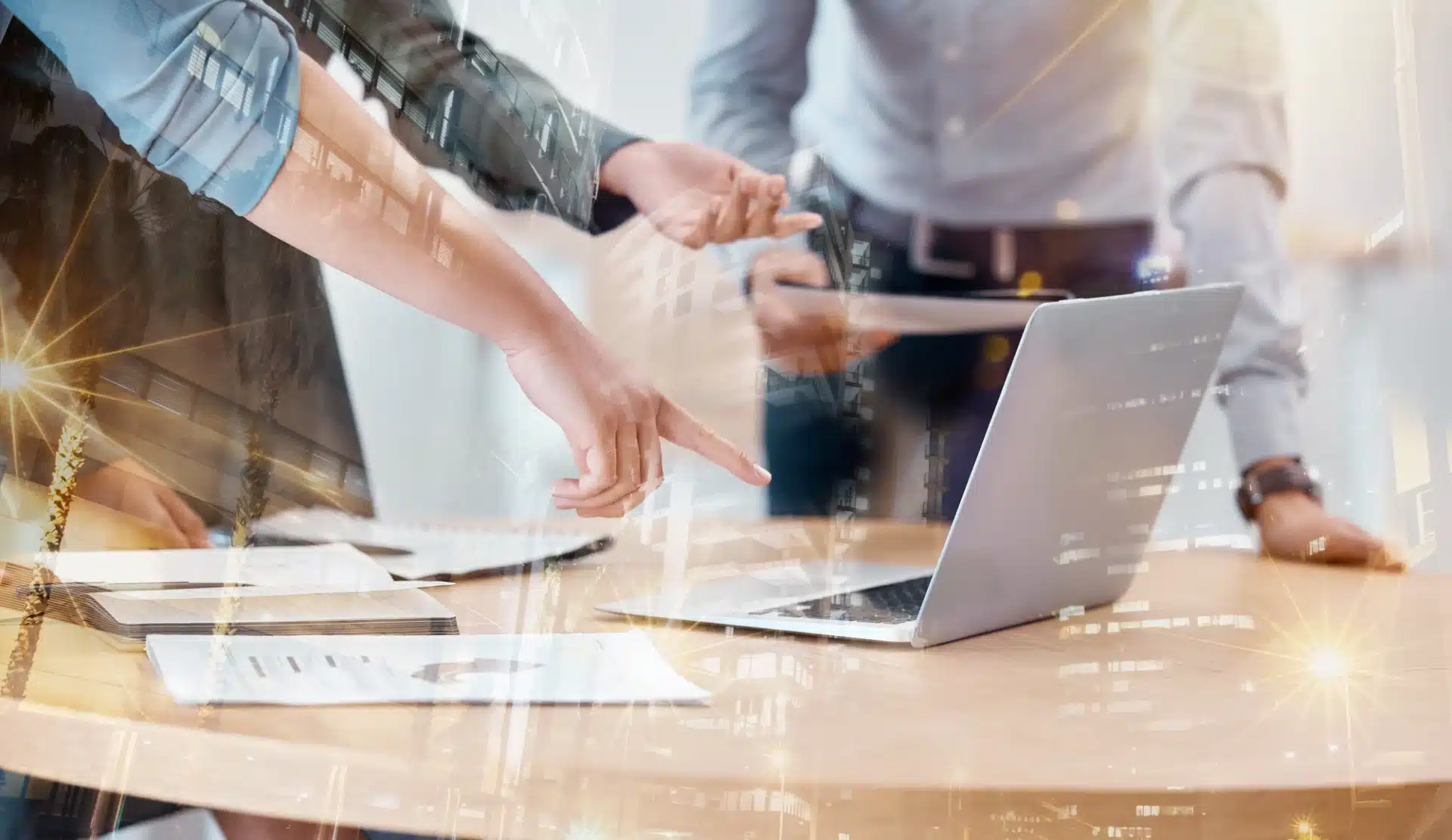 Hands pointing at a laptop during a business meeting, with documents and notes visible on a table, symbolizing collaboration in digital marketing strategies.
